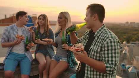 Loving-young-russian-couples-sit-on-the-roof-and-drink-beer-with-pizza.-They-enjoy-a-beautiful-sunset-and-time-with-their-mate.